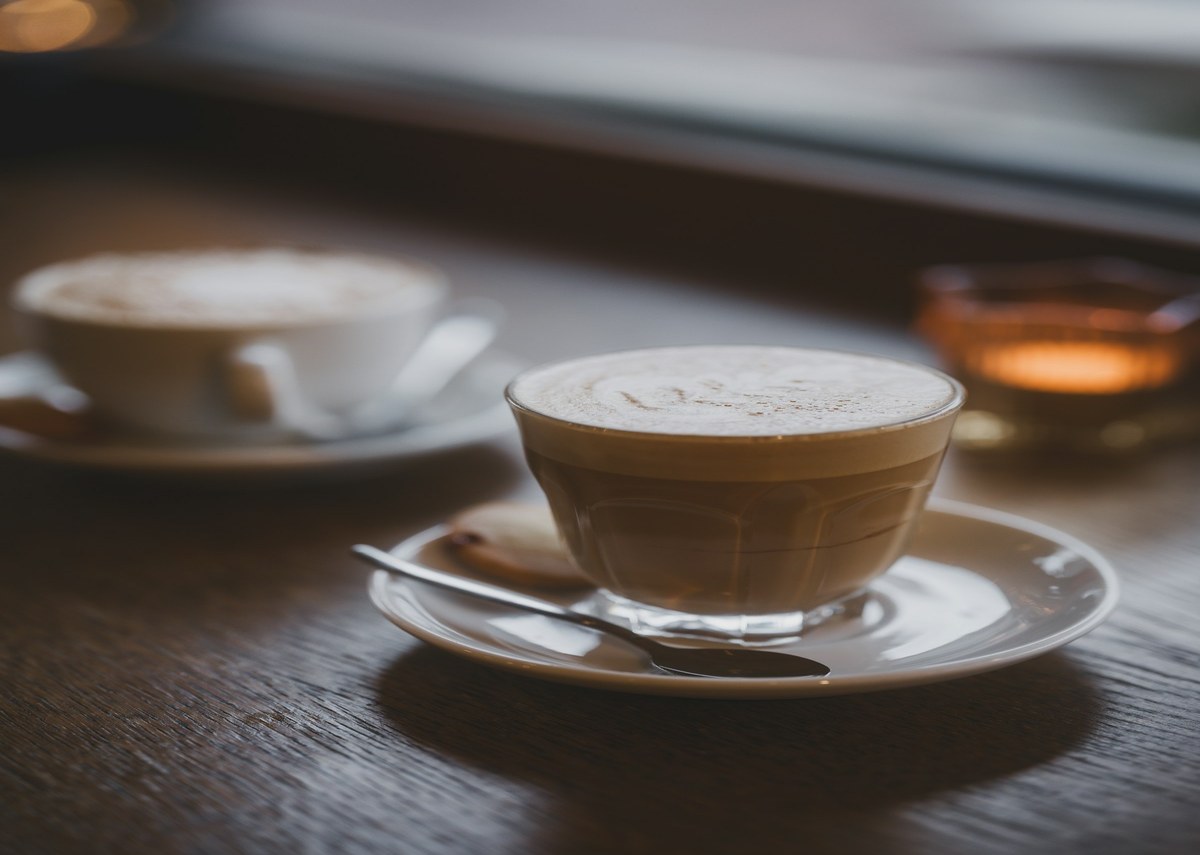 Cappuccino and cortado on a wooden cafe table beside a lit candle