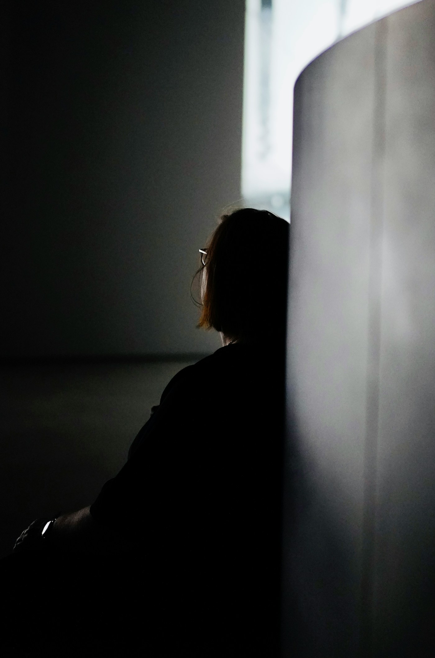 Woman sitting alone in a dim room beside a wall