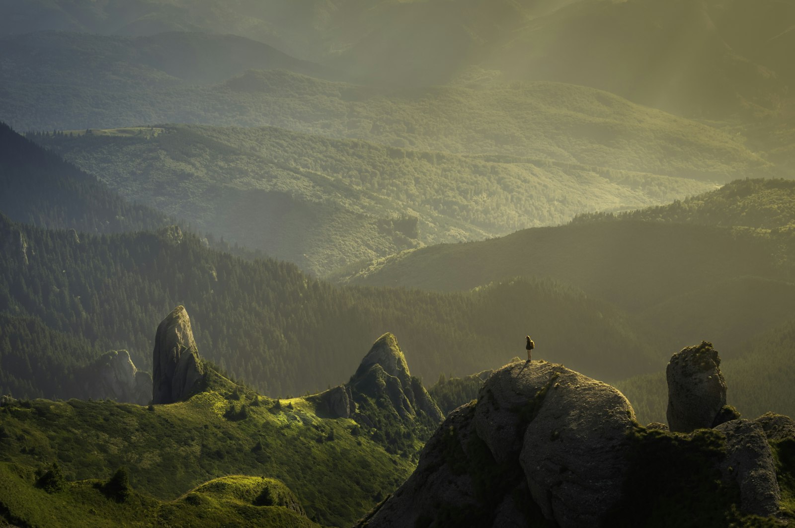 A solitary person standing on a rocky peak looking out over misty mountains