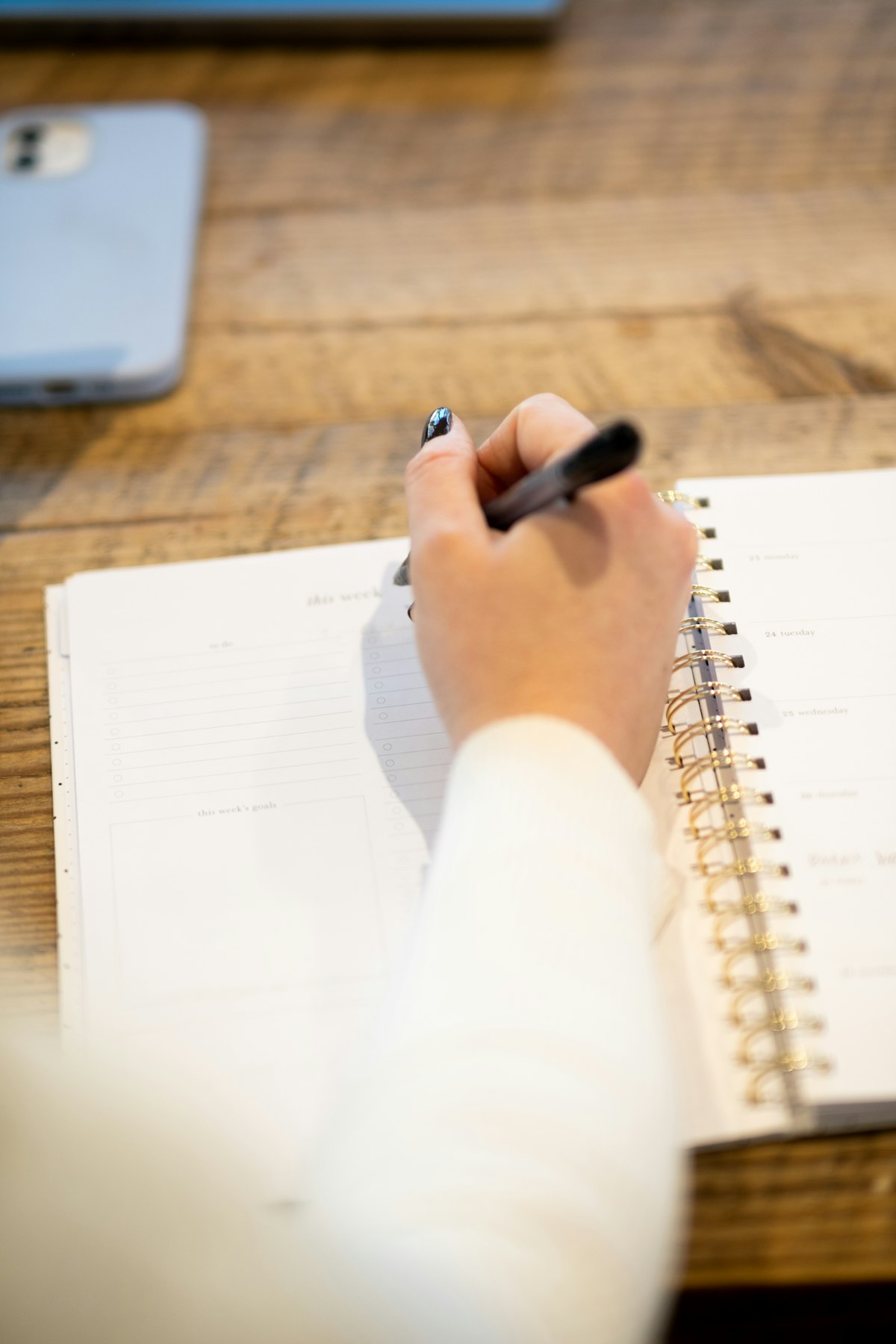Person writing in a planner on a wooden table