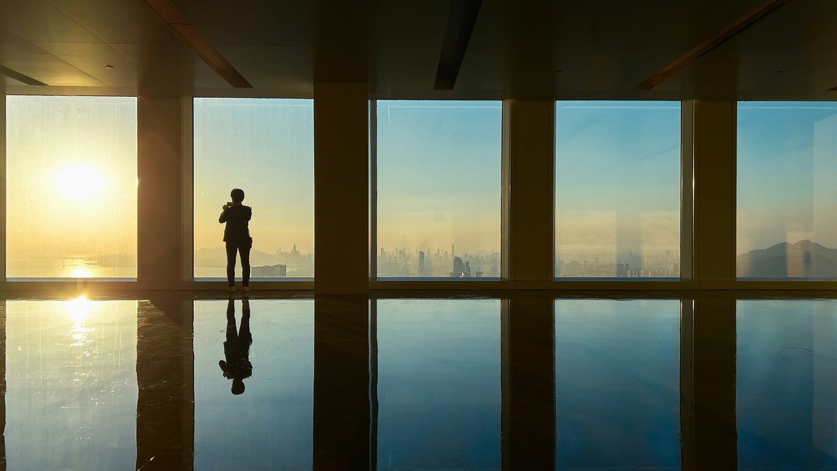Person silhouette standing in front of large windows at sunrise, city skyline behind them