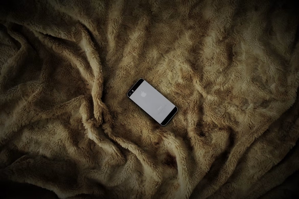 A smartphone lying face-down on a textured brown blanket, seen from above
