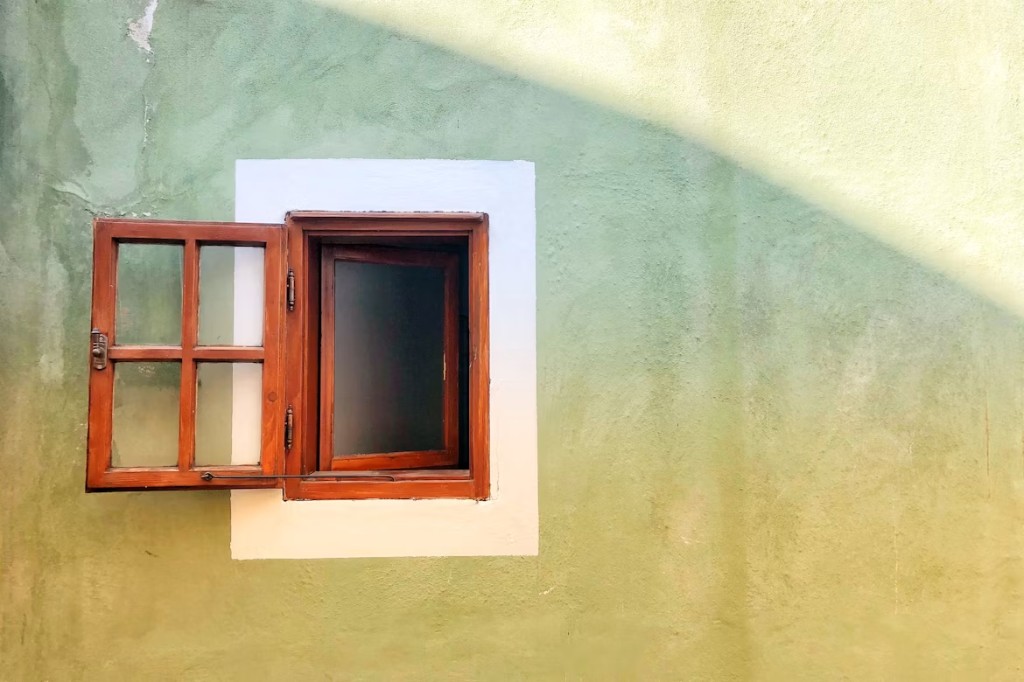 A wooden window swung open on a sunlit green wall