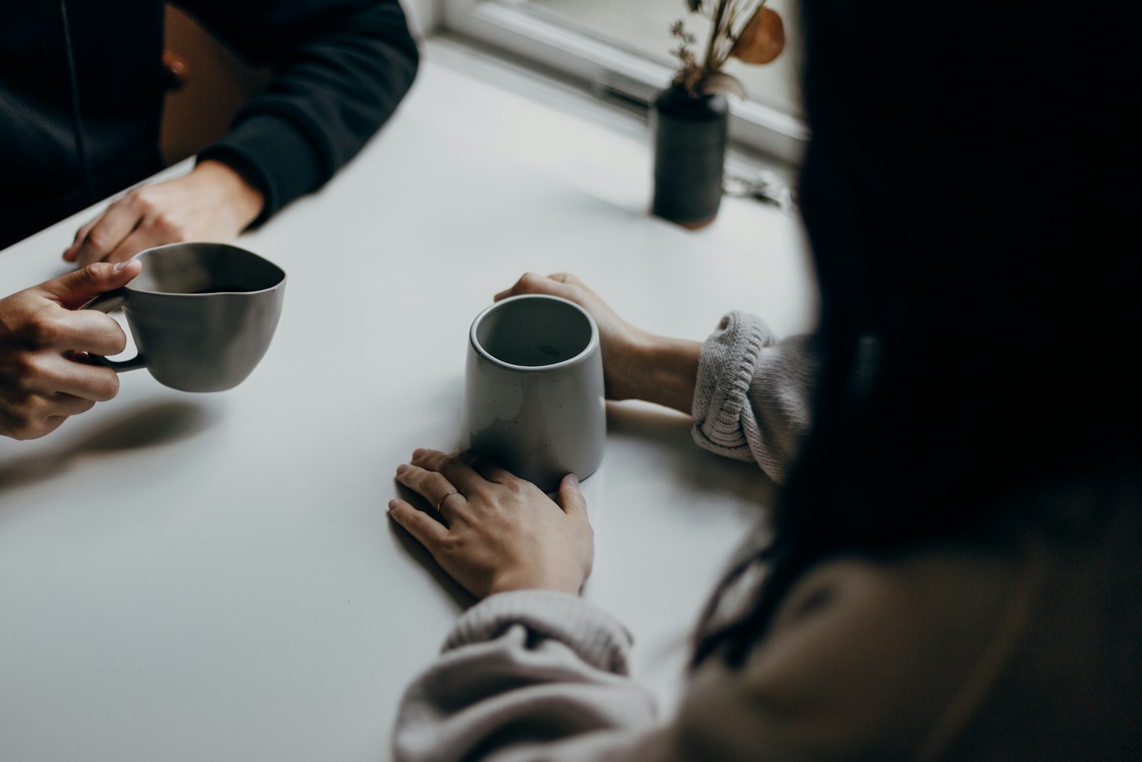 Two people holding mugs of coffee together at a table