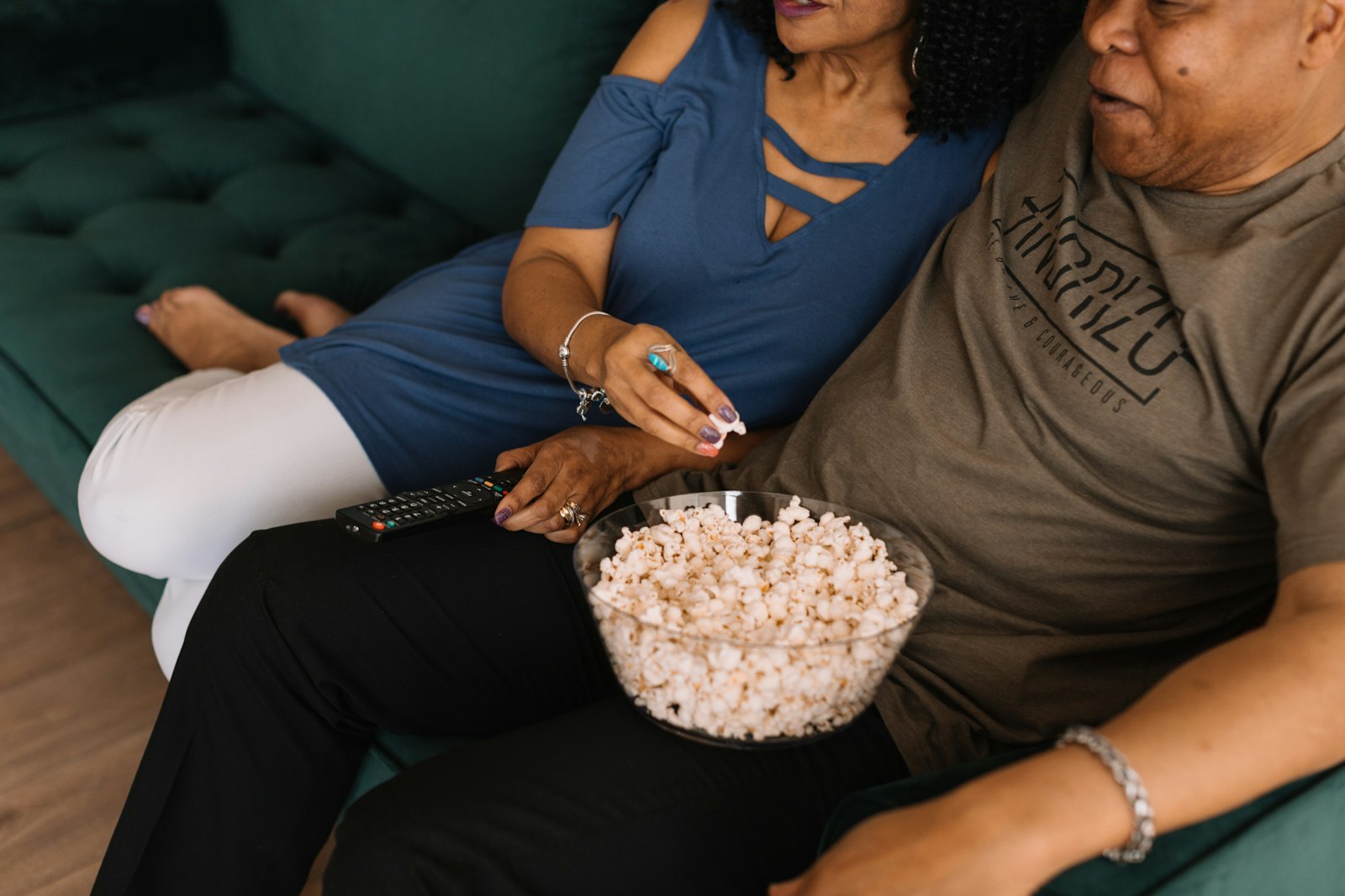 A couple sitting together on a couch, sharing popcorn while watching a movie