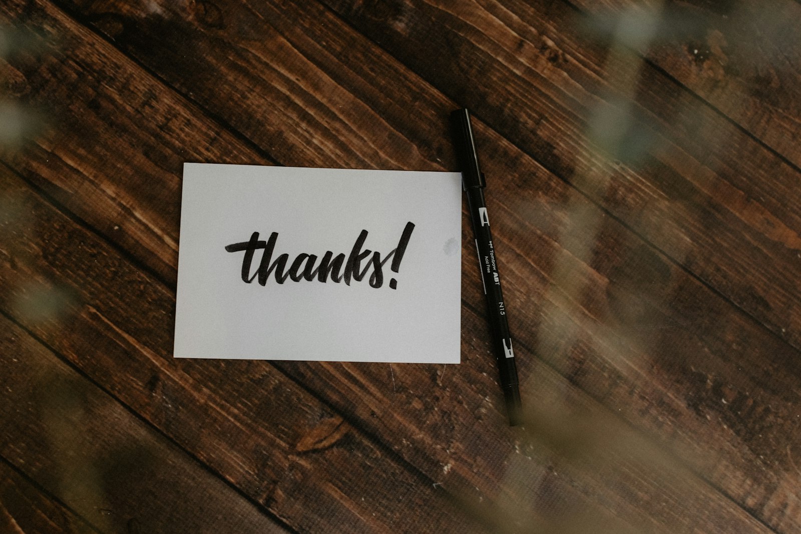 A handwritten "thanks!" note and pen on a wooden surface