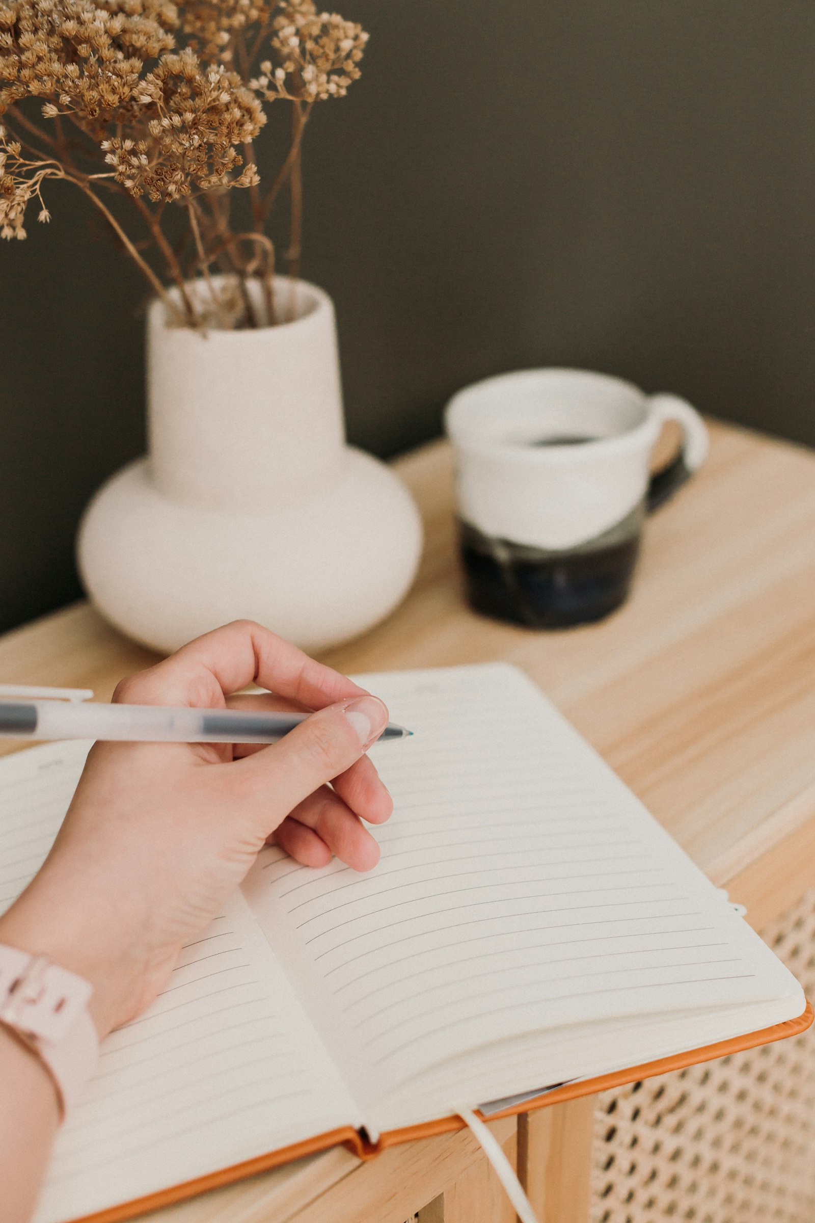 Hand writing in an open notebook beside a cup of coffee